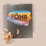 16.10.2023: Das Föhr-Heft auf einem hellen Hintergrund, darauf das Heft, Cover schwarz mit einem farbenfrohen Bild mit Schriftzug "Föhr", darunter Herbstdeko Strauch